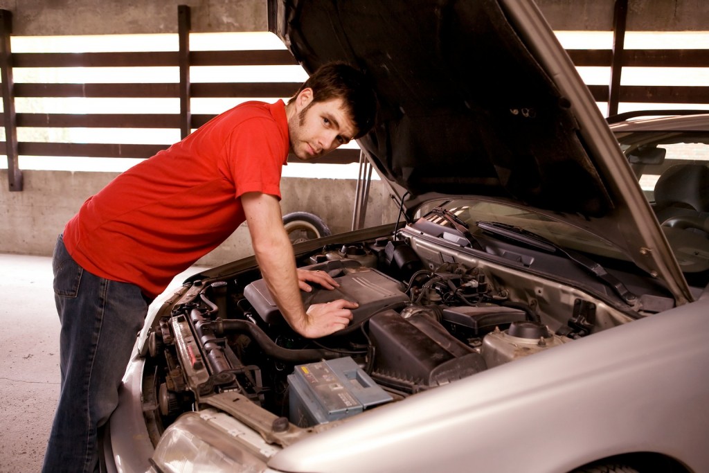 A male looking under the hood of a car